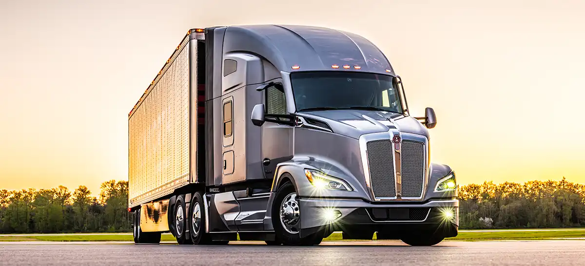 A Kenworth T680 Next Gen semi truck with a sunset in the background.