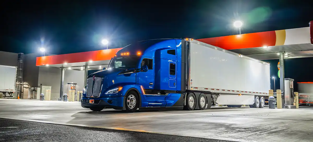 A Kenworth T680 parked at a gas station at night.