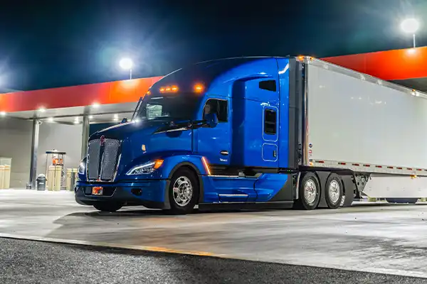 A blue Kenworth T680 parked at a gas station at night.