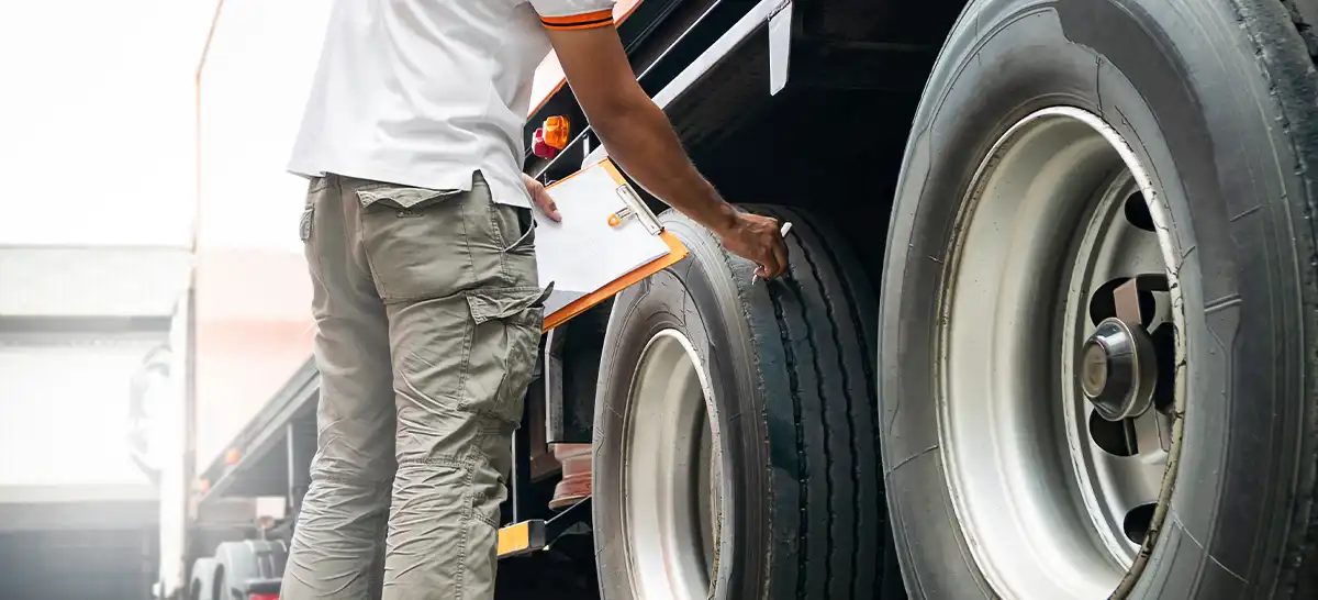 A man is conducting a safety check on the wheels of a semi-truck.